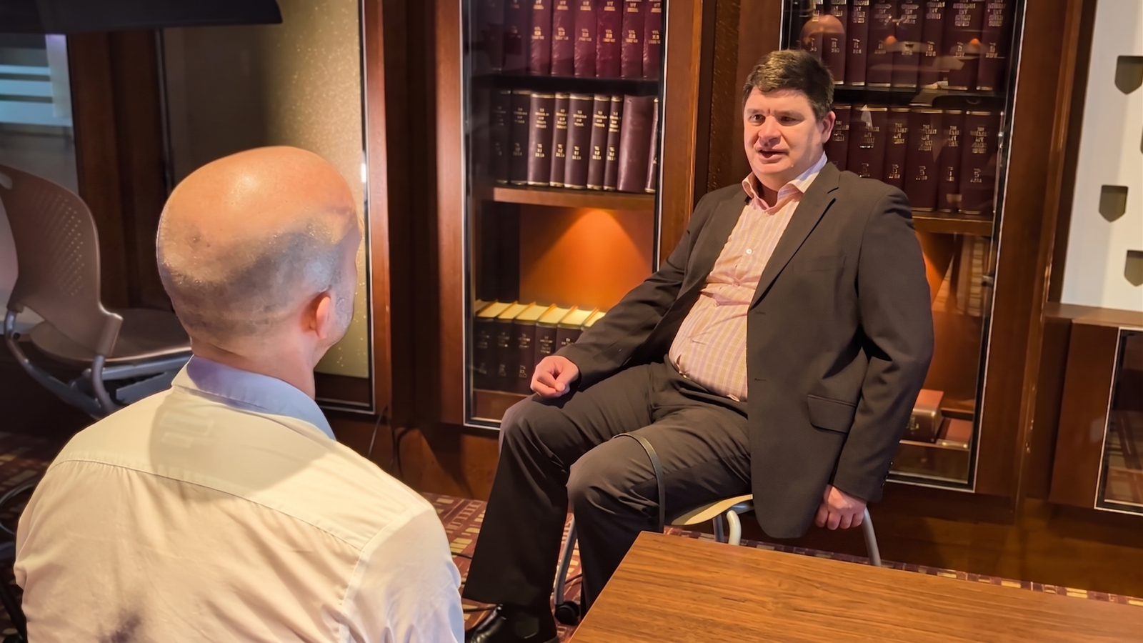 Professor Paul Harpur, seated in front of shelves of law reports, mid-conversation with Luke Angel, who sits opposite with his back to the camera.